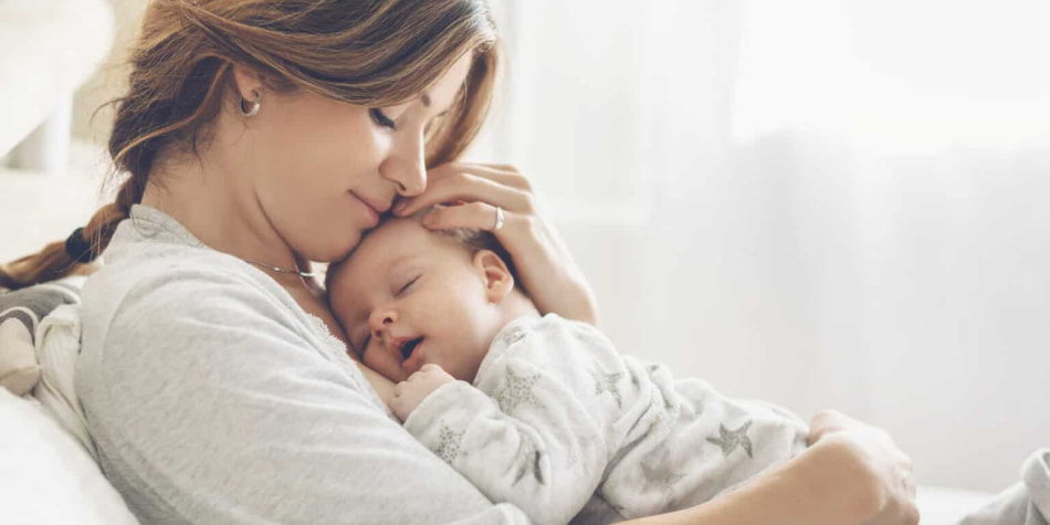 A mom snuggles her newborn baby, cradling his head as she lays the
    infant against her chest.