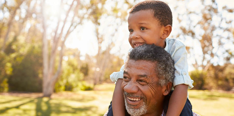 A grandfather carries his grandson on his shoulders.